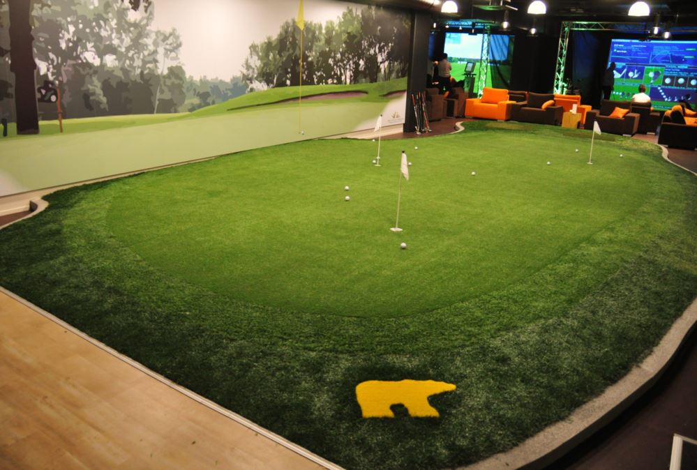 Large indoor putting green with artificial turf and multiple practice holes, designed for year-round golf training inside a modern entertainment space.
