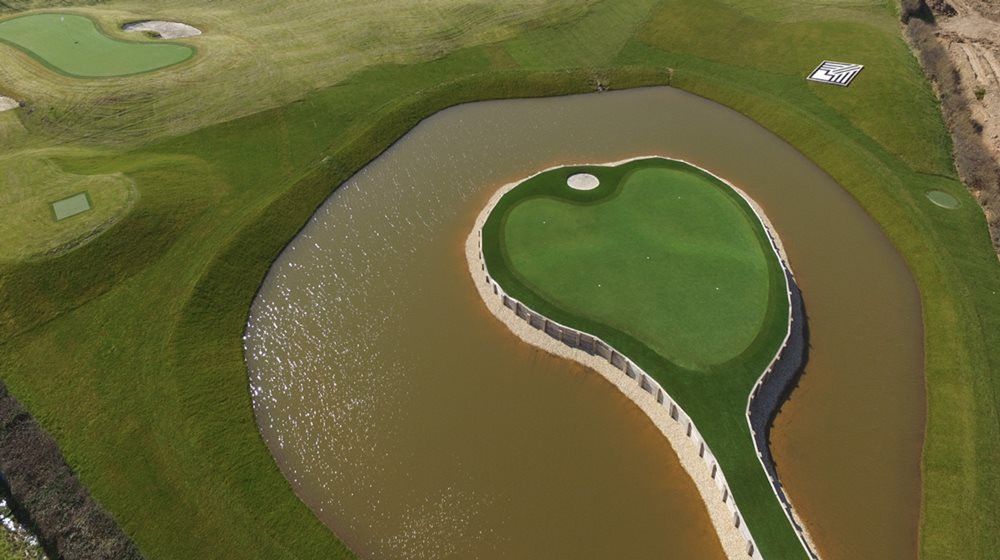 Asheville Aerial view of a vibrant green synthetic grass island in a natural pond on a golf course