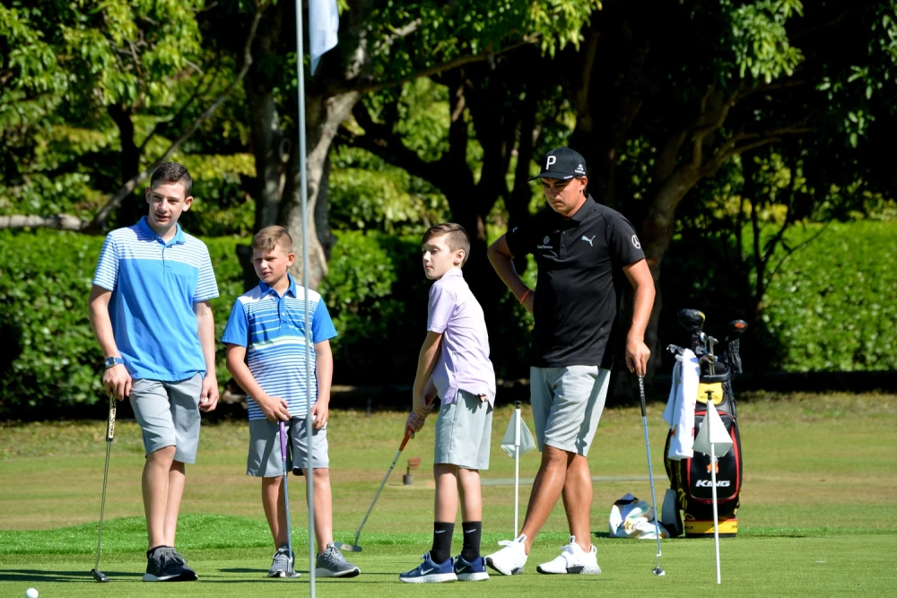 Rickie Fowler practicing on a backyard putting green with three junior golfers